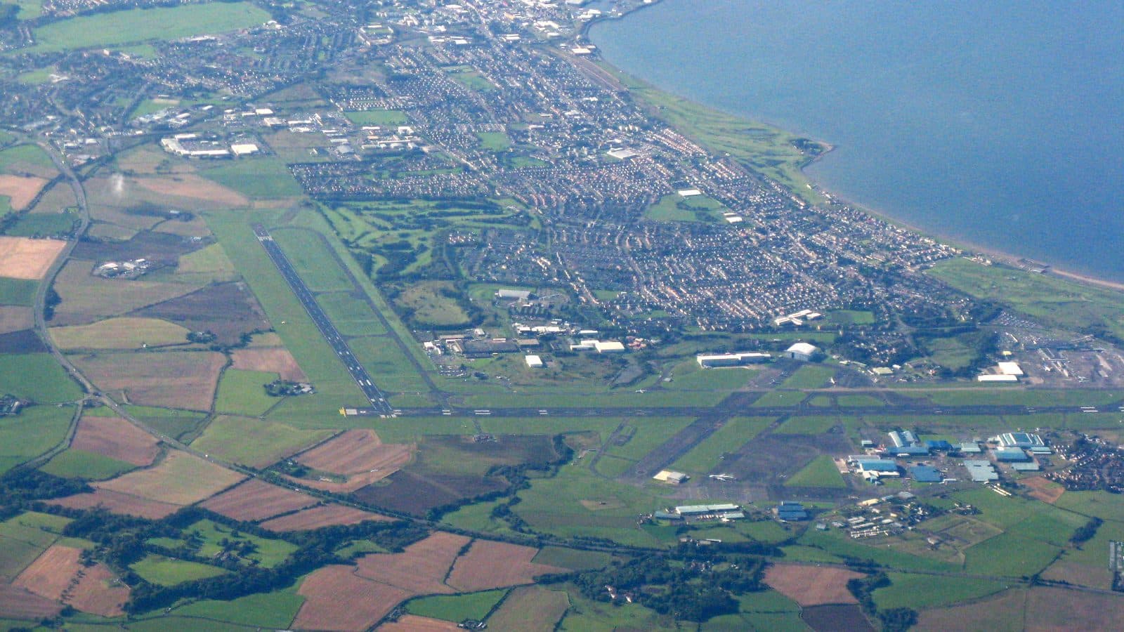 Aerial view of Prestwick, Scotland, and its airport: runways, farmland, the town and the coastline